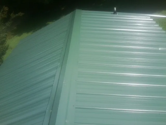 New green metal panels meeting at the ridge of a roof — Flat Roof Repair work by our crew in Prague