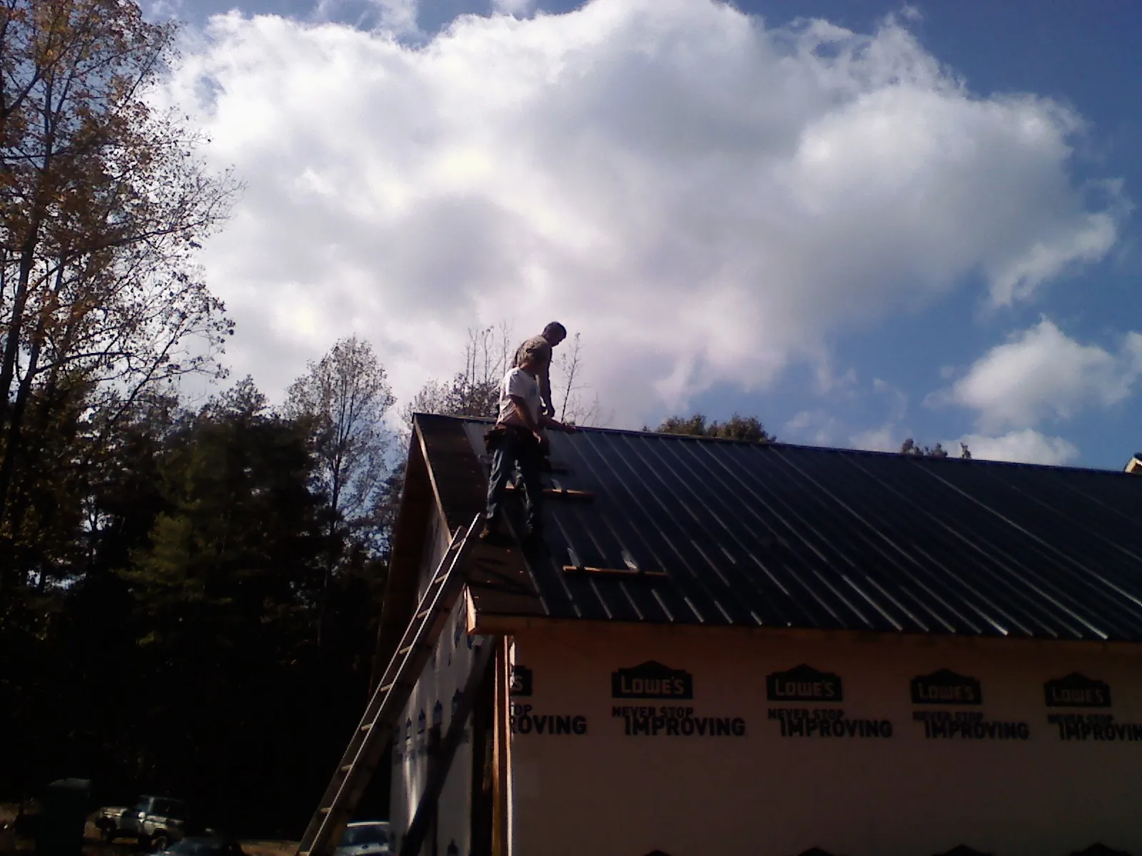 Roofer fastening dark metal panels high against a cloudy sky, from a Roof Inspection job in Prague