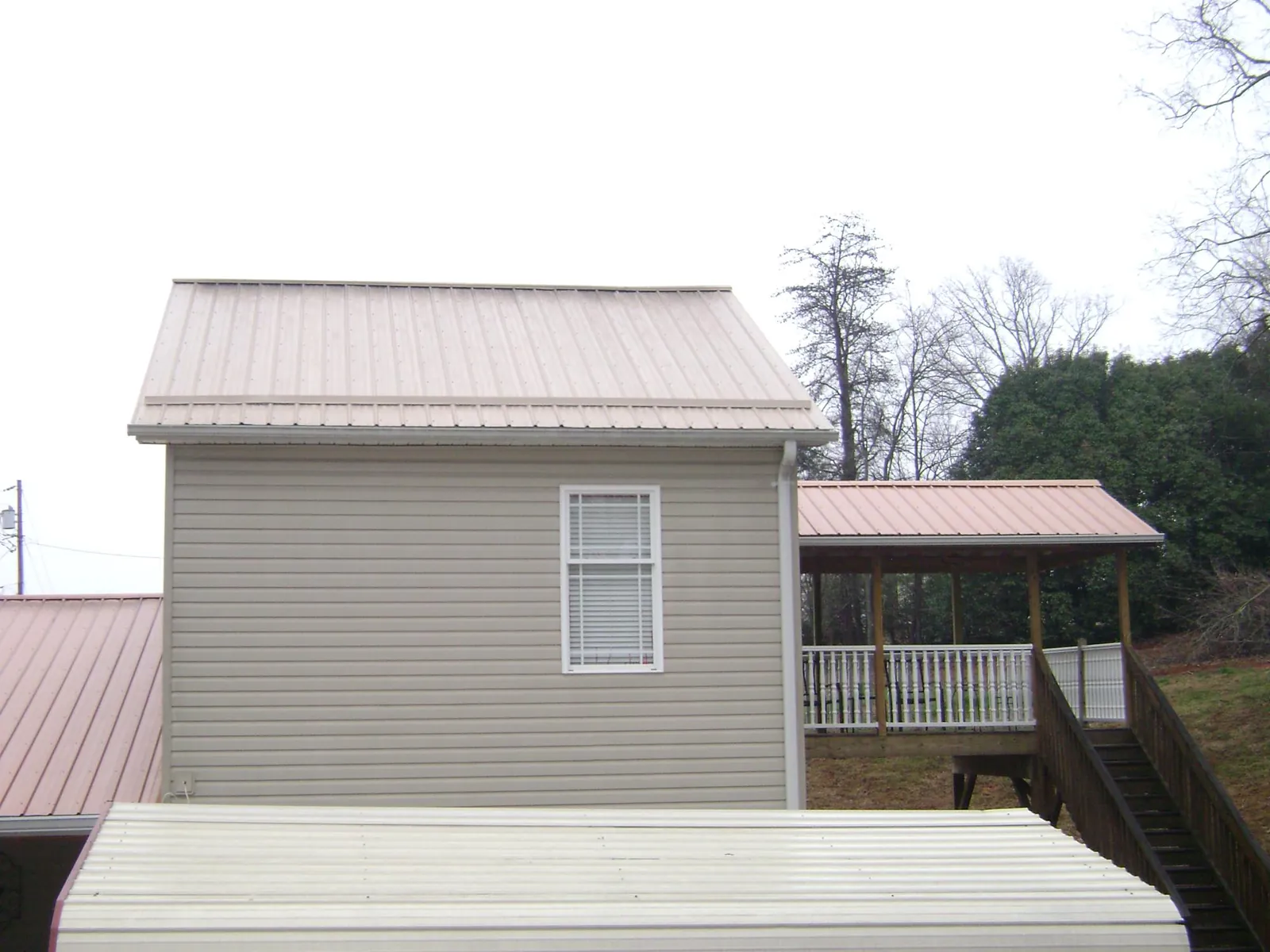 Tan metal roofs on a two story addition and attached porch, from a Roof Replacement job in Prague